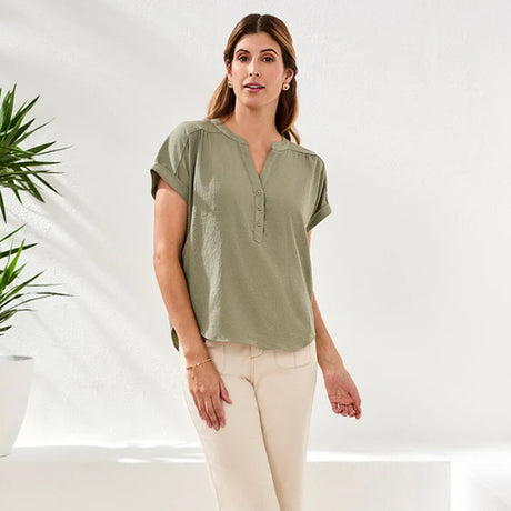 Woman wearing an olive green shirt and beige pants against a white background