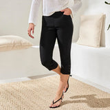 Person wearing black capri pants in a minimalistic room with white walls and beige pillows.