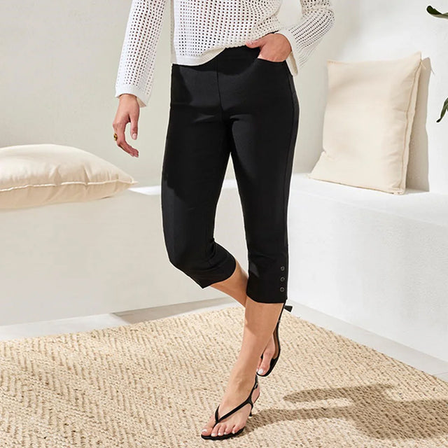 Person wearing black capri pants in a minimalistic room with white walls and beige pillows.