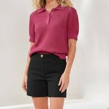 Person wearing a pink textured polo shirt and black shorts on a plain background