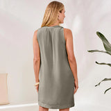 Woman wearing a sleeveless green dress standing in a room with a plant.