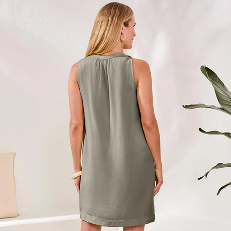 Woman wearing a sleeveless green dress standing in a room with a plant.