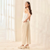 Woman wearing a white sleeveless top and beige pants standing in a softly lit room.