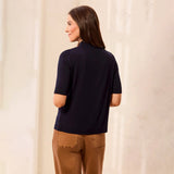 A woman shown from the back wearing a dark navy short-sleeve knit top and brown pants, standing against a light cream textured wall.