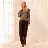 A woman stands in a bright indoor room wearing a marled brown knit sweater, dark brown pants, and brown shoes.