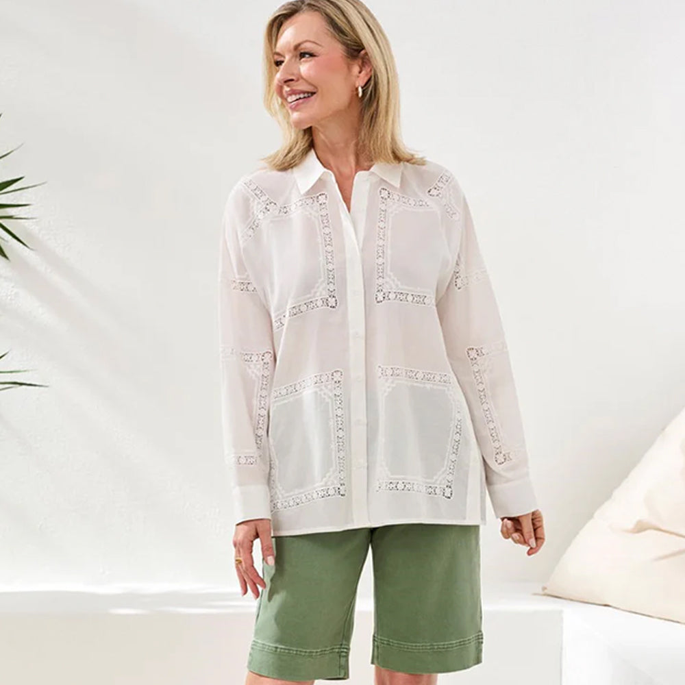 Woman wearing a white embroidered blouse and green pants on a white background