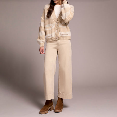 Person wearing a beige cardigan, white shirt, and pants with brown shoes on a plain background