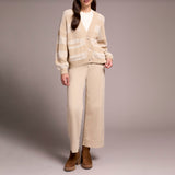 Person wearing a beige cardigan and pants with brown shoes on a plain background