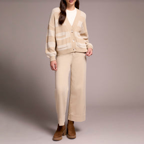 Person wearing a beige cardigan and pants with brown shoes on a plain background