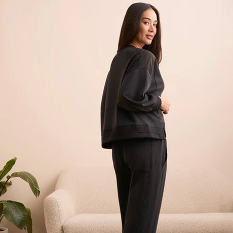 Woman wearing a black outfit standing in a room with a beige wall and a plant.
