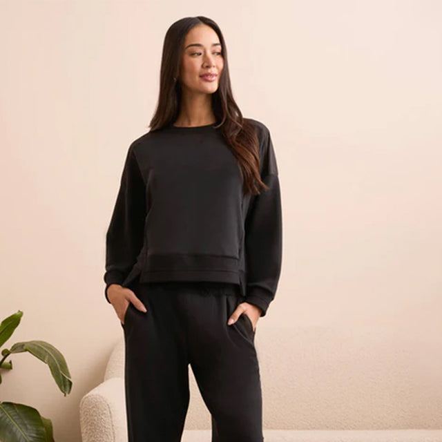 Woman wearing a black outfit against a beige wall