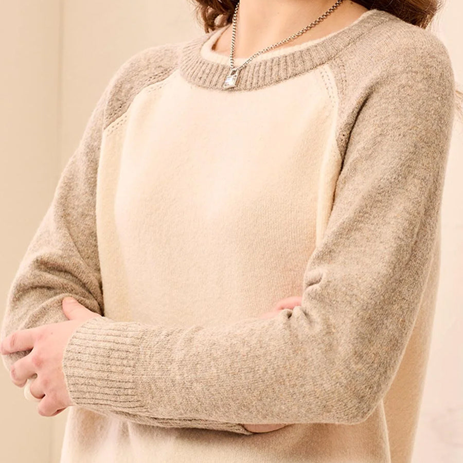 A close-up of a woman wearing a knit sweater with a cream center panel and taupe-beige raglan sleeves and collar. The sweater has a fine knit texture and ribbed cuffs and hem.