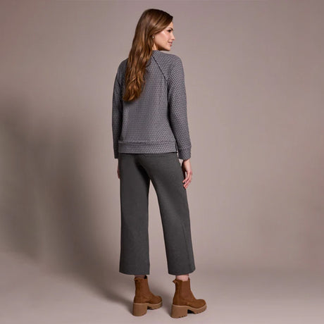 Woman wearing a gray textured jacket and pants with brown boots against a beige background