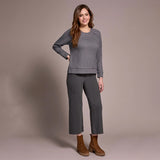 Woman wearing a gray patterned top and pants with brown boots against a beige background