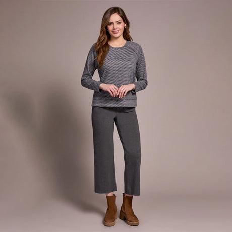 Woman wearing a gray sweater and pants with brown boots on a beige background