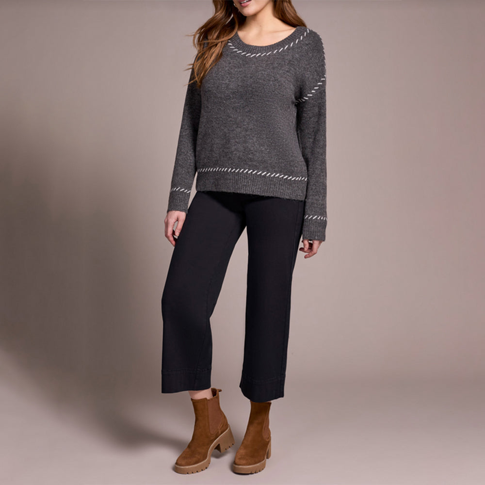 Person wearing a gray sweater, black pants, and brown boots on a plain background