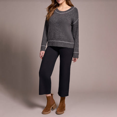 Person wearing a gray sweater, black pants, and brown boots on a plain background