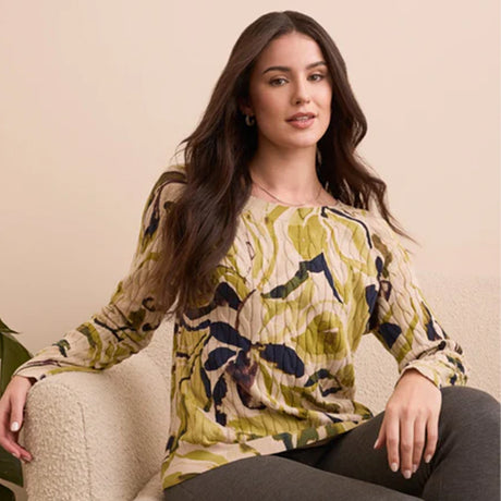 Woman wearing a floral blouse sitting on a beige chair against a beige background