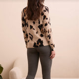 Person wearing a leopard print sweater and gray pants against a beige wall.
