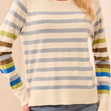 A woman wearing a cream-colored knit sweater with horizontal blue-gray, olive green, brown, blue, and white stripes on the sleeves and hem.