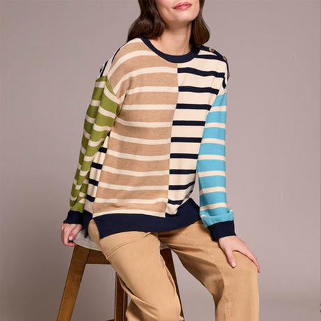 Person wearing a multicolored striped sweater and beige pants on a plain background