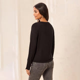 A woman shown from the back wearing a black long-sleeve top and gray jeans, standing against a light cream-colored backdrop.