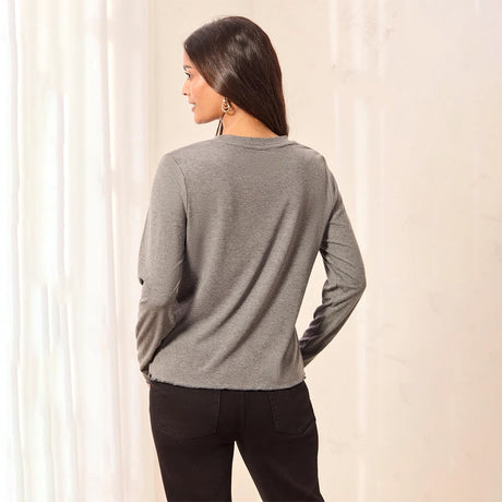 A woman shown from the back wearing a heather gray long-sleeve top and black pants, standing indoors against a light curtain background.