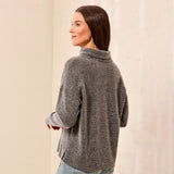 A woman wearing a textured gray knit mock neck sweater, shown from a three-quarter back view against a neutral cream-colored wall.