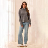 A woman stands in a softly lit room wearing a heather gray knit mock-neck sweater, light-wash blue jeans, and white sneakers.