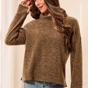 A woman wearing a textured, long-sleeve knit mock neck sweater in a warm brown and beige heathered pattern, paired with blue jeans.