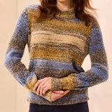 A woman wearing a marled knit sweater with horizontal stripes in blue, beige, and brown tones, cropped from the chin down against a plain beige background.