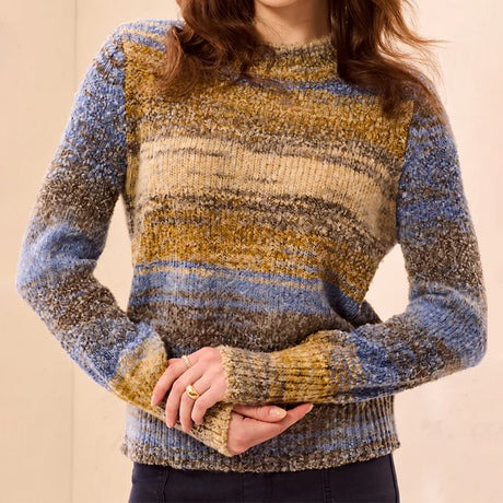 A woman wearing a marled knit sweater with horizontal stripes in blue, beige, and brown tones, cropped from the chin down against a plain beige background.