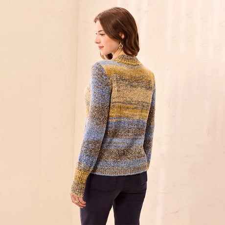 A woman shown from the back wearing a marled knit sweater with horizontal stripes in blue, yellow, and brown tones, paired with dark pants, set against a neutral cream-colored background.