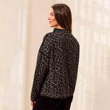 A woman wearing a black and gray leopard print fleece jacket, shown from a side-back angle against a warm, sunlit cream-colored wall.