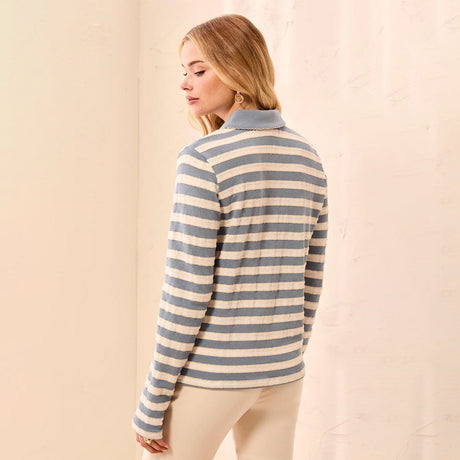 A woman wearing a long-sleeve knit polo-style top with horizontal blue-gray and cream stripes, shown from the back against a soft beige backdrop.