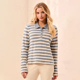 A woman modeling a long-sleeve polo shirt with horizontal gray and cream stripes, paired with light beige pants, set against a warm beige textured wall.