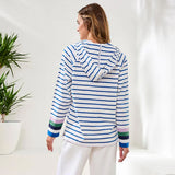 Woman wearing a blue and white striped hoodie with colorful cuffs and hem, standing in a minimalistic room.