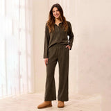 A woman modeling a matching two-piece lounge set in a warm, softly lit room. The set consists of a long-sleeve button-front top and matching wide-leg pants, both in a textured olive-brown fabric.