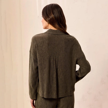 A woman shown from the back wearing a textured, dark olive green long-sleeve top and matching pants against a neutral cream-colored wall.