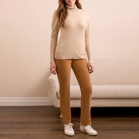 Person wearing a beige sweater and brown pants standing in a room with a beige couch.