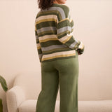 Person wearing a striped sweater and green pants in a neutral setting