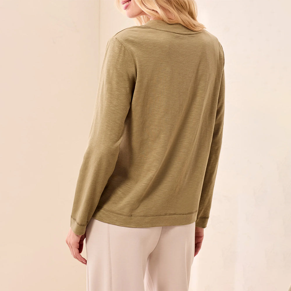 A woman shown from the back wearing a long-sleeve olive green top and light beige pants against a soft beige studio background.