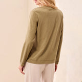 A woman shown from the back wearing a long-sleeve olive green top and light beige pants against a soft beige studio background.