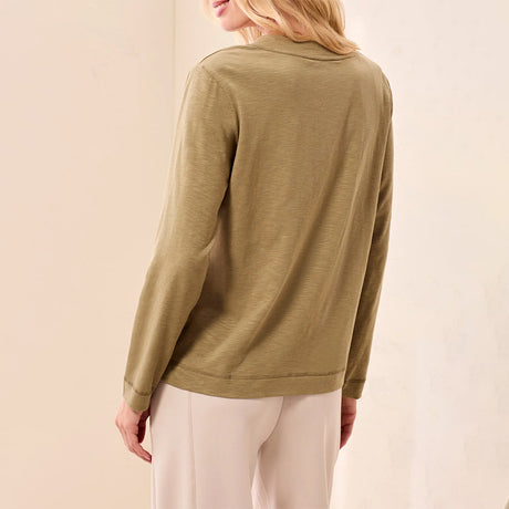 A woman shown from the back wearing a long-sleeve olive green top and light beige pants against a soft beige studio background.