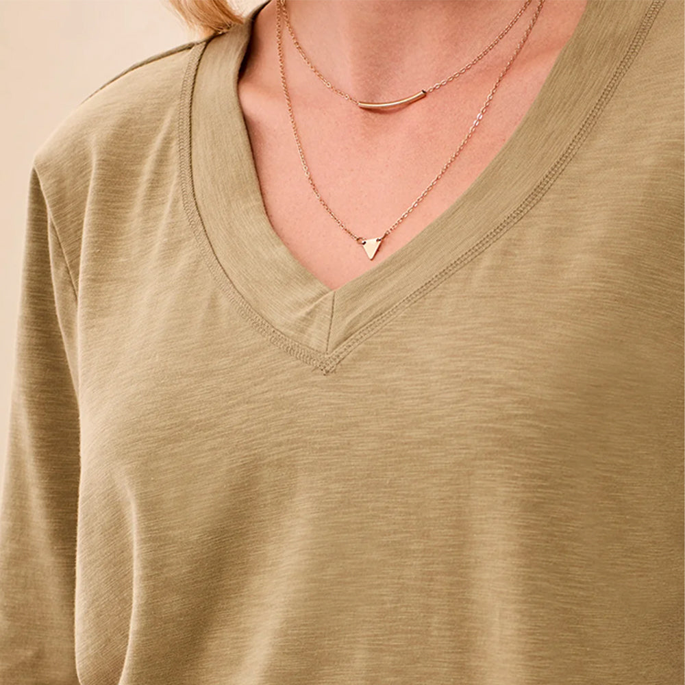 Close-up of a person wearing a light olive-beige V-neck long-sleeve top with layered delicate necklaces.