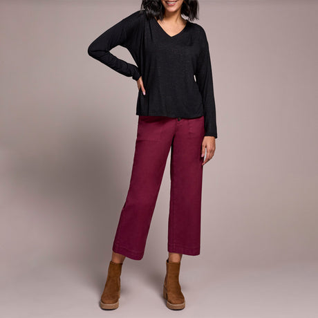 Person wearing a black top and maroon pants with brown boots on a plain background