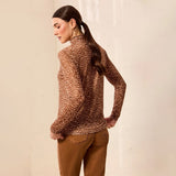 A woman wearing a brown and beige leopard-print mock neck sweater and brown pants, photographed from the back against a light beige wall.