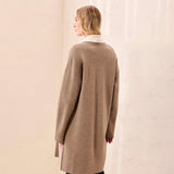 A woman shown from the back wearing an oversized taupe knit cardigan with a contrasting cream collar, standing against a textured off-white wall.