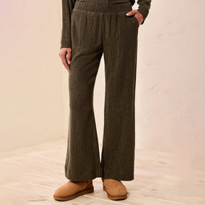 A person wearing dark olive green wide-leg knit pants with a matching long-sleeve top and tan suede boots, standing against a light beige wall and tiled floor.