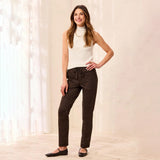 A woman modeling dark brown leopard-print pants with a drawstring waist, paired with a white ribbed sleeveless top and black flats, standing in a bright indoor setting with sheer curtains.